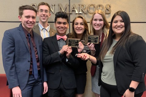 Group of students holding awards with "Howard Payne University" sign in the background. | HPU