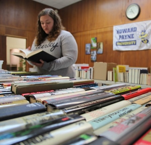 Woman browsing books at a Howard Payne University sale or library. | HPU