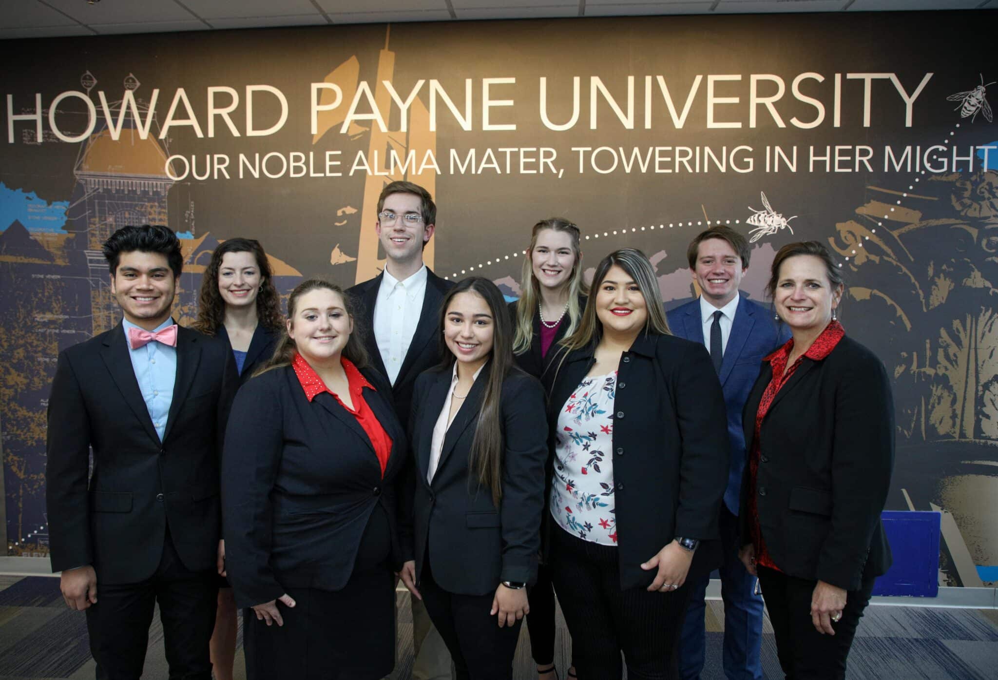 A group of nine individuals smiling for a photo at Howard Payne University, with the university's slogan in the background. | HPU