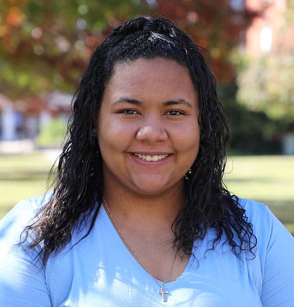 A smiling woman with wet hair outdoors wearing a Howard Payne University blue top and a cross necklace. | HPU