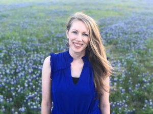 A woman in a blue top, smiling in a field of bluebonnets near Howard Payne University. | HPU