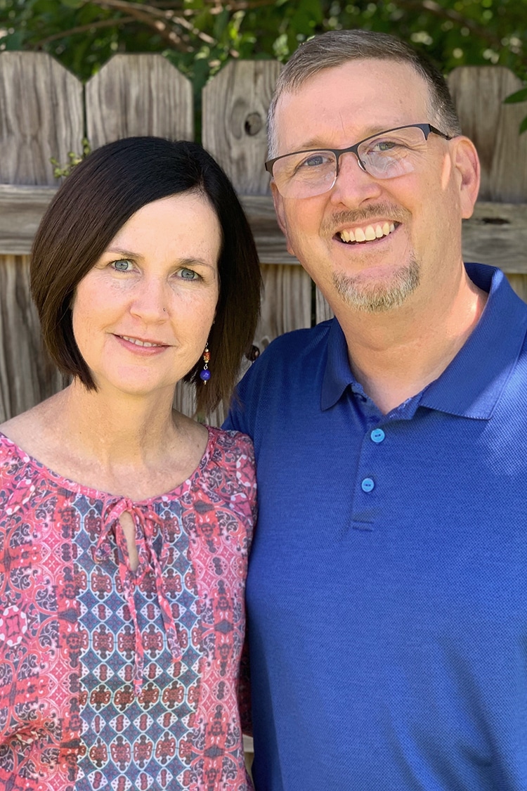 A smiling couple posing together in front of a wooden fence at Howard Payne University. | HPU