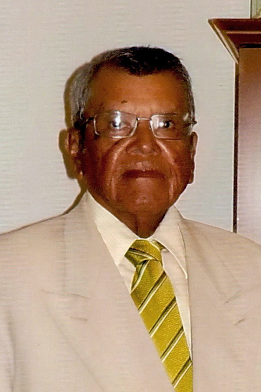 An older man in a beige suit and striped tie standing indoors at Howard Payne University. | HPU