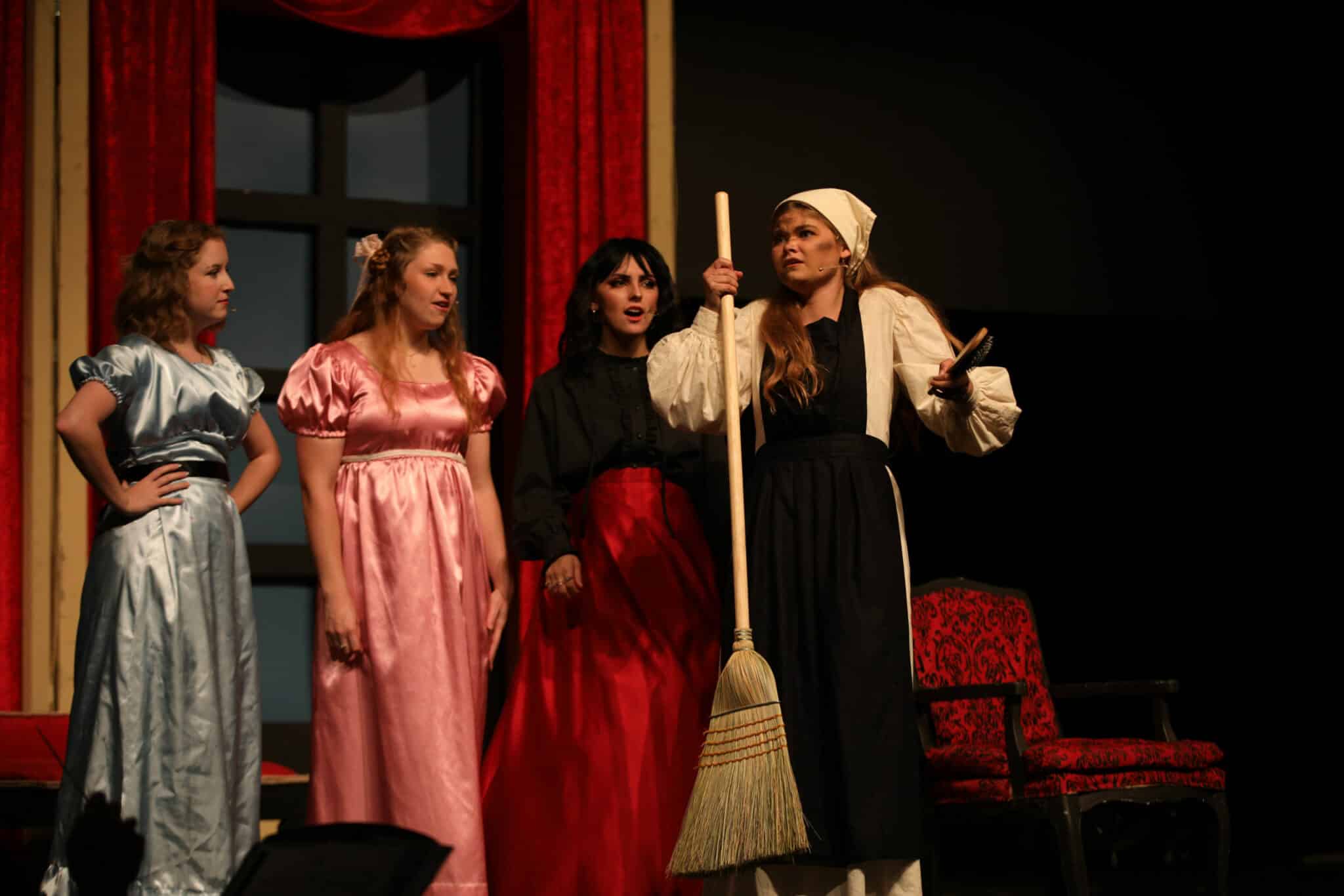 Four actors on stage in Howard Payne University period costumes, with one holding a broomstick, performing in a theatrical production. | HPU