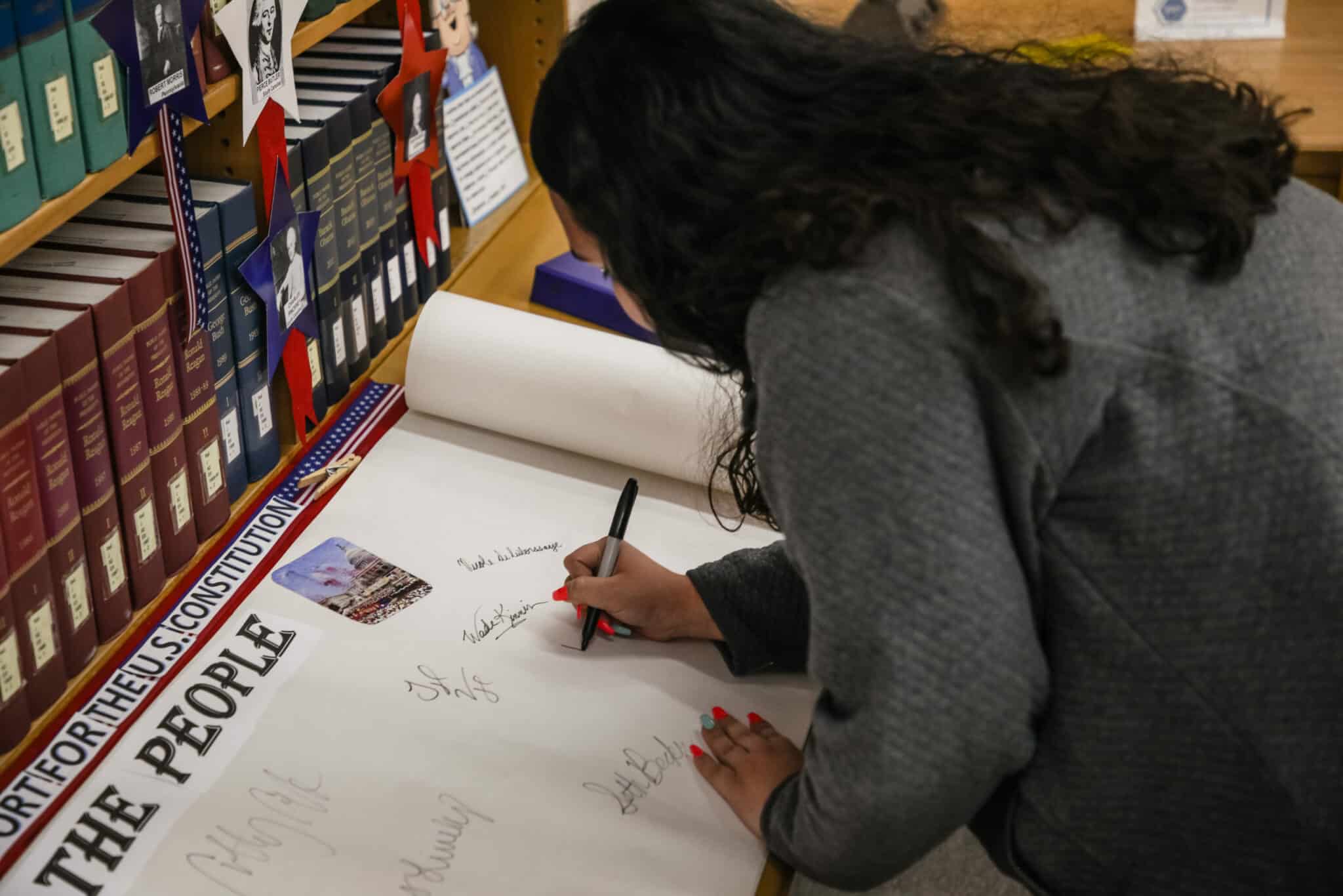 A person signing a document on a table with books and informational posters about Howard Payne University in the background. | HPU