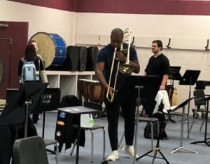 A trombonist practicing in a Howard Payne University band room with empty chairs and music stands around him. | HPU