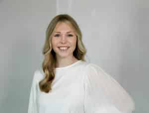 A smiling woman with long hair in a Howard Payne University top against a grey background. | HPU
