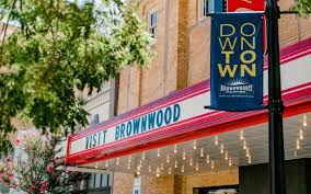 A marquee over a sidewalk with dangling lights reads "visit Brownwood" beneath a banner that says "downtown Brownwood, near Howard Payne University. | HPU