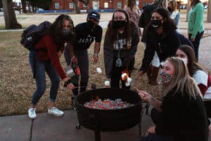 Group of Howard Payne University students wearing face masks roasting marshmallows over a fire pit. | HPU