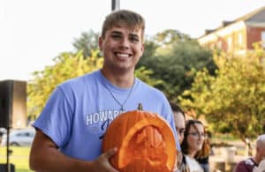 A smiling person holding a carved pumpkin outdoors at a Howard Payne University social event. | HPU