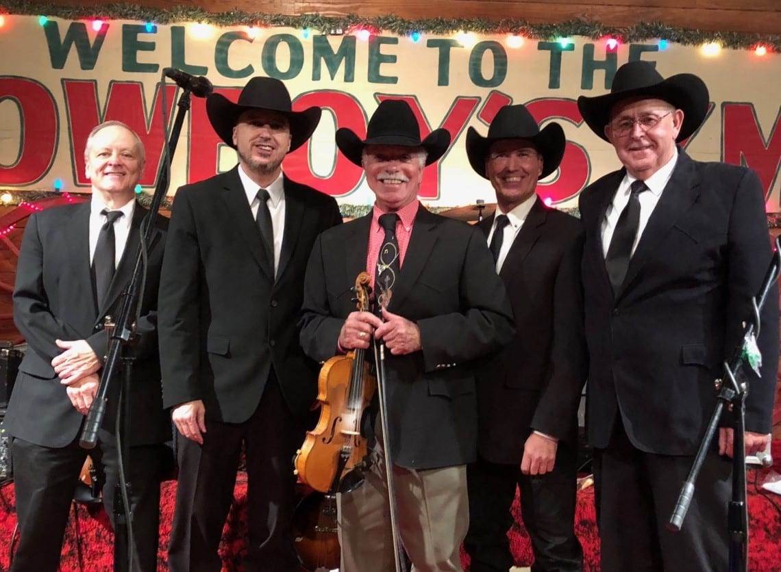 Five men in cowboy hats smiling for a photo at an event with a "welcome to the Howard Payne University cowboy church" banner in the background. | HPU