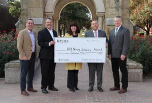 Group of five individuals from Howard Payne University posing with a large ceremonial check for a nursing scholarship, outdoors amidst greenery. | HPU