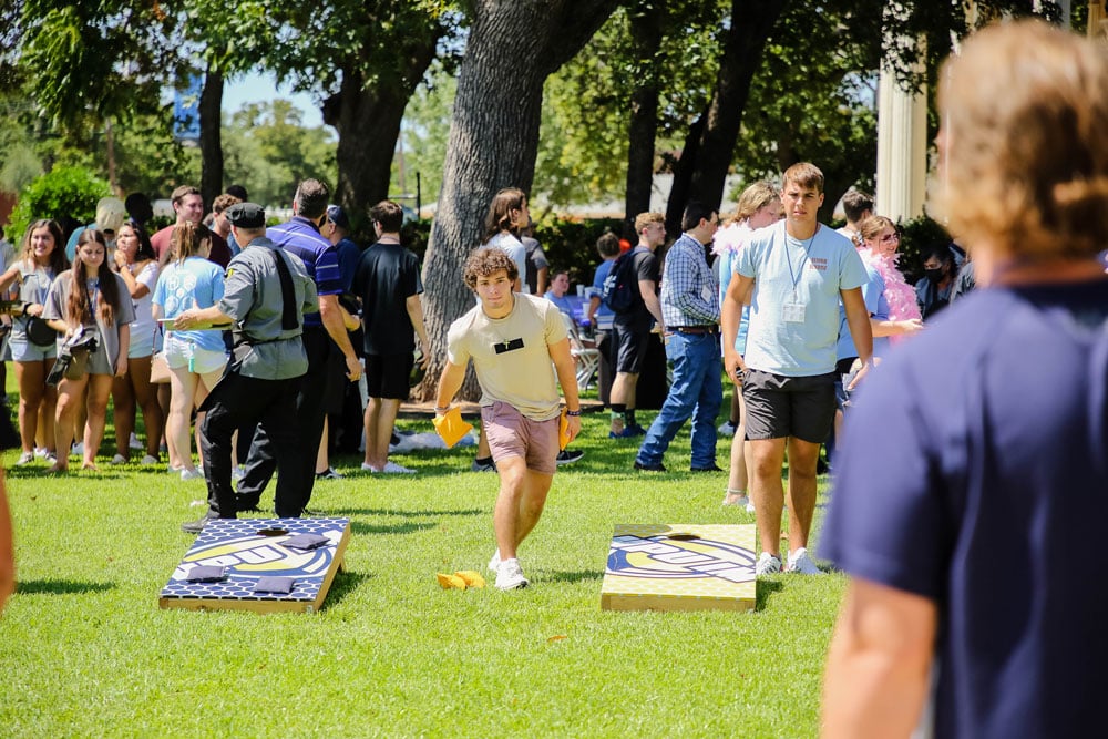 Group of Howard Payne University students participating in an outdoor cornhole game on a sunny day. | HPU