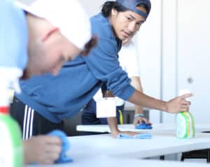A Howard Payne University student cleaning a surface with a spray bottle and cloth while focusing intently on the task. | HPU