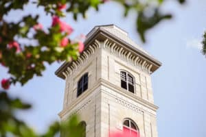 Stone tower with a red window framed by foliage against a clear sky at Howard Payne University. | HPU
