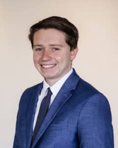 A smiling person in a Howard Payne University blue suit with a purple tie. | HPU