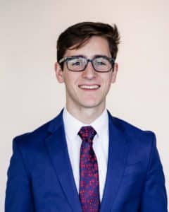Young man in Howard Payne University blue suit and patterned tie smiling at the camera. | HPU
