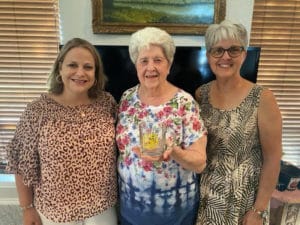 Three smiling women posing for a photo together indoors at Howard Payne University, with the central woman holding a glass. | HPU