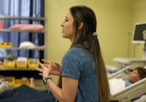A female student at Howard Payne University in a clinical setting appears to be engaged in a discussion or presentation. | HPU