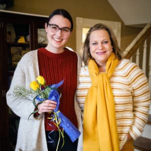 Two women posing indoors at Howard Payne University, one holding a bouquet of flowers, both smiling at the camera. | HPU