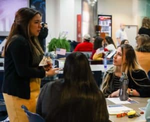A woman speaking to seated individuals at a Howard Payne University event with American flags on the tables. | HPU