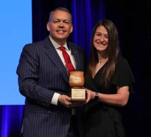 A man in a striped suit and a woman in a black dress, both representing Howard Payne University, holding an award together and smiling. | HPU