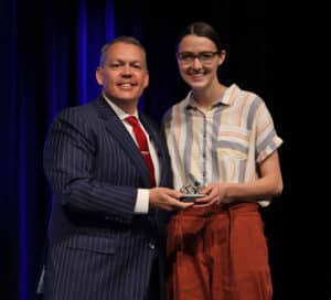 A man in a striped suit and a woman in a striped shirt, both from Howard Payne University, smiling and holding an award together onstage. | HPU