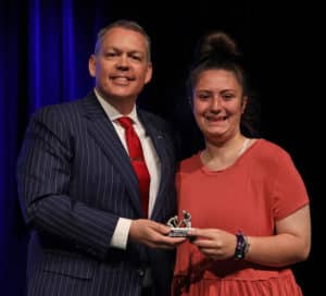 A man in a pinstripe suit presenting an award to a smiling young woman on the Howard Payne University stage. | HPU
