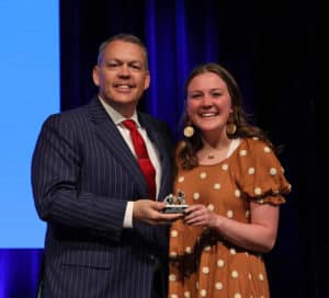 Man in a striped suit and woman in a polka-dot dress, both from Howard Payne University, smiling and holding an award together. | HPU