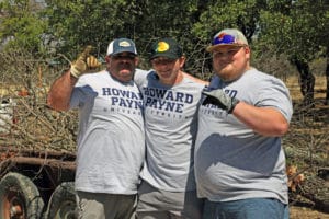 Three individuals wearing matching Howard Payne University t-shirts and gloves posing for a photo outdoors. | HPU