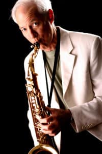 Man in a white jacket playing a saxophone against a dark background at Howard Payne University. | HPU