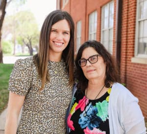 Two women smiling outdoors, one standing slightly behind the other, in front of a brick building at Howard Payne University. | HPU