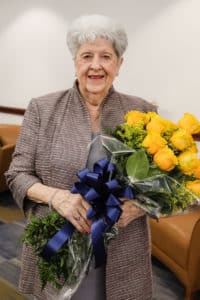 An elderly woman smiling, holding a bouquet of yellow roses with a blue ribbon, representing Howard Payne University. | HPU