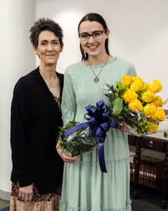 Two women smiling for a photo at Howard Payne University, one holding a bouquet of yellow roses with a blue ribbon. | HPU