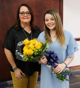 Two women smiling and posing for a photo at Howard Payne University, with the younger woman holding a bouquet of yellow flowers. | HPU