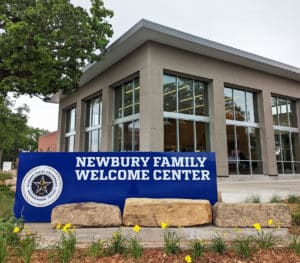 Modern building with a sign reading "Howard Payne University Newbury Family Welcome Center" surrounded by landscaping with yellow flowers. | HPU