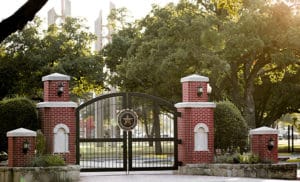 An ornamental gate with brick pillars at the entrance of Howard Payne University, basked in warm sunlight. | HPU
