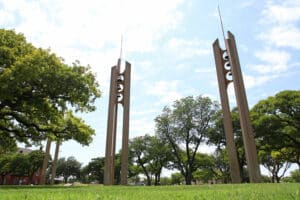 Three vertical sculptures at Howard Payne University park under a clear sky with lush green trees in the background. | HPU