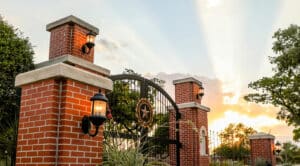 A warm sunset skies behind ornate metal gates flanked by brick pillars with Howard Payne University lanterns. | HPU