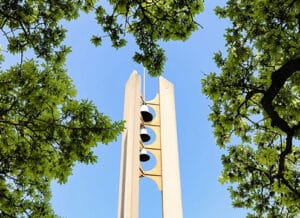 A modern bell tower at Howard Payne University framed by green trees against a clear blue sky. | HPU
