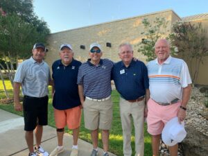 Five smiling men posing together outdoors at Howard Payne University's golfing event. | HPU