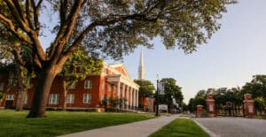 Howard Payne University campus at sunset with a red-brick building and tree-lined pathway. | HPU