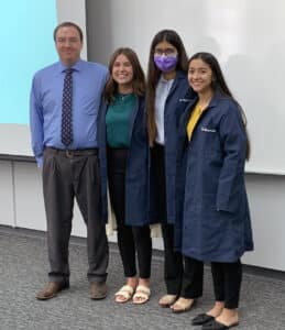 Four individuals posing for a photo in a Howard Payne University classroom setting, two of whom are wearing lab coats. | HPU