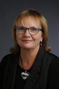 A professional headshot of a smiling woman with glasses and a Howard Payne University heart-shaped necklace. | HPU