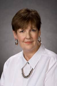 A professional headshot of a woman with short hair wearing a white shirt and a Howard Payne University pearl necklace. | HPU