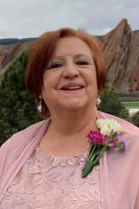 A smiling woman with a flower corsage, wearing a pink dress and shawl, with rocky formations in the background at Howard Payne University. | HPU