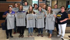 Group of smiling people proudly displaying t-shirts with 'Howard Payne University Alumni' printed on them. | HPU