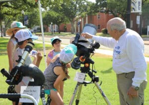A group of people from Howard Payne University using a telescope outdoors on a sunny day with an instructor guiding them. | HPU