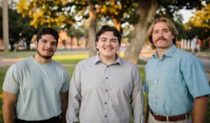 Three smiling men posing outdoors in Howard Payne University's park. | HPU