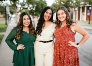 Three smiling women posing together outdoors at Howard Payne University. | HPU